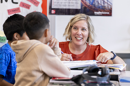 A teacher works with two students at their desks